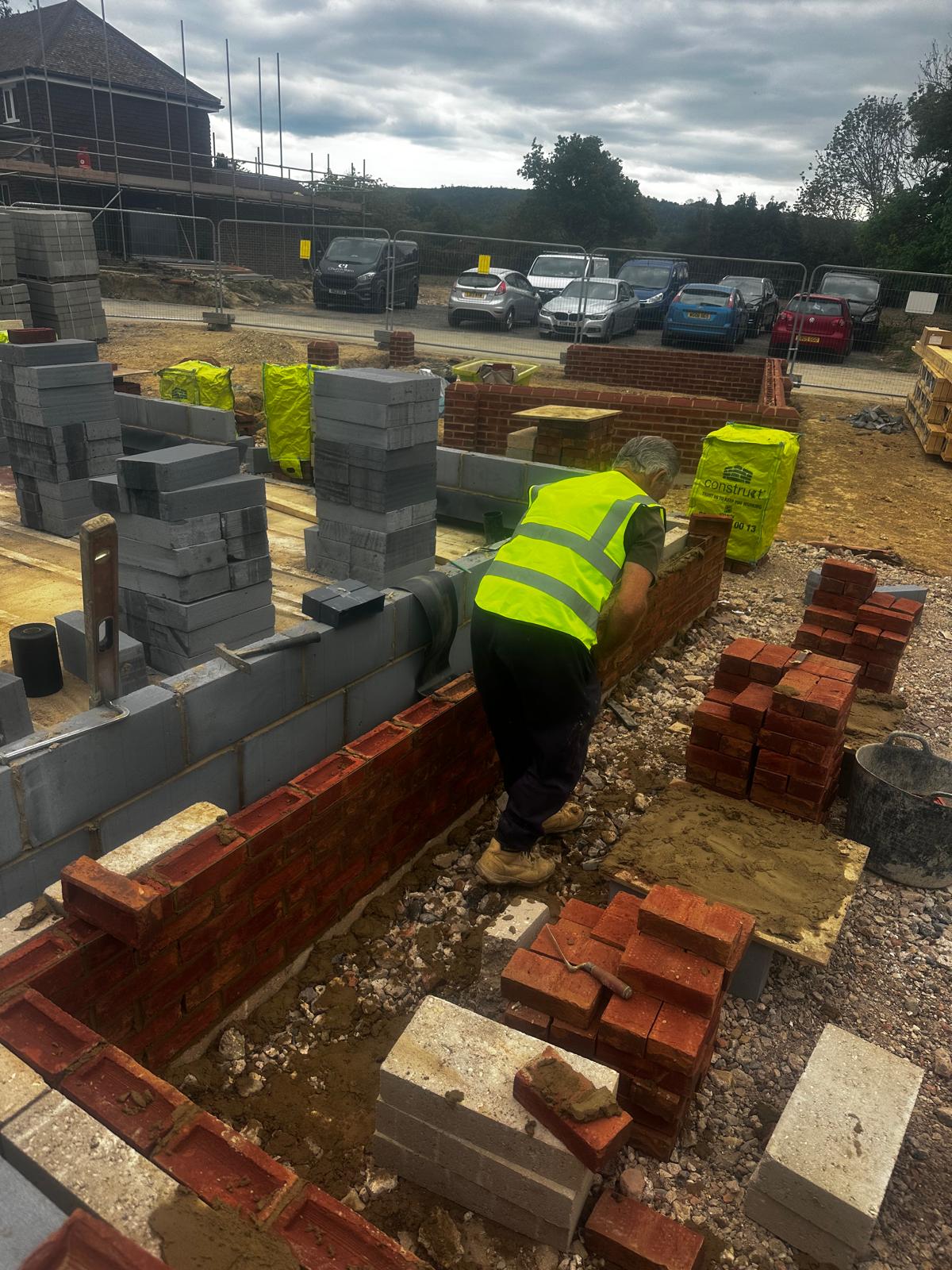 Bricklayer setting the first brick course on blockwork footings